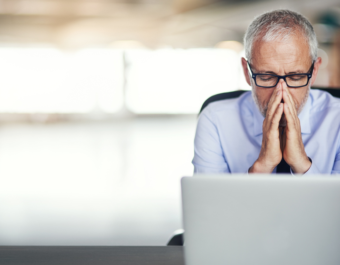 An older worker sits stressed out in front of his laptop. (stock image)