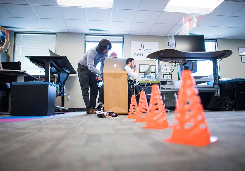 Ramses Alcaide working with a Neurable staffer demonstrates how the technology works to move a Lego Mindstorm toy car by interpreting brain activity at the startup's office space at SPARK in Ann Arbor this summer. Photo by Austin Thomason, Michigan Photography.