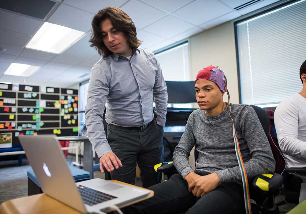 Ramses Alcaide working with a Neurable staffer demonstrates how the technology works to move a Lego Mindstorm toy car by interpreting brain activity at the startup's office space at SPARK in Ann Arbor this summer. Photo by Austin Thomason, Michigan Photography.