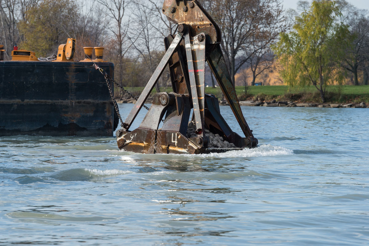 Loaded buckets were lowered to the river bottom before the rock was released. The latest Belle Isle reefs are located in water that is 18 to 22 feet deep, and they rise about 2 feet above the river bottom. About 4 acres of new rock reefs were created and are located outside commercial shipping channels. Image credit: Austin Thomason, Michigan Photography