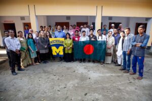 School of Public Health delegates, FCAB members, kids and villagers of Bagdumur come together to hold University of Michigan and Bangladesh flags.