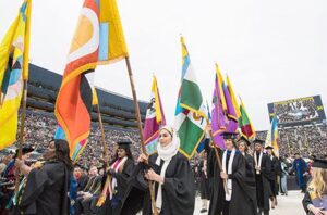 Graduates enter Michigan Stadium bearing the flags of U-M's schools and colleges. (Photo: Austin Thomason, Michigan Photography.)