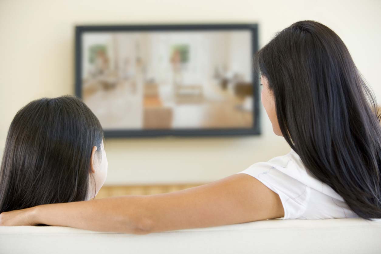 Woman and young girl in living room with television. (stock image)