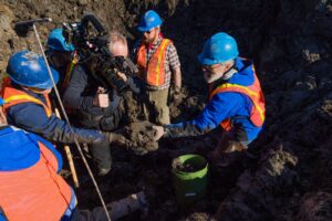 Paleontologist Daniel Fisher, right, hands a mammoth vertebra to Michael Cherney as a film crew records the exchange.