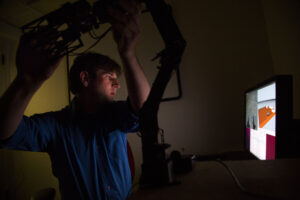 Steve Vozar, ME PhD Student, tests one of the Unmanned Ground Vehicles (UGV) he is working on in the HH Dow Building on October 15, 2013. Traditionally, unmanned ground vehicles (UGVs) are tele-operated with a joystick, and with real-time video feedback information gathered from a camera on the UGV. When there isn't a direct line-of-sight from the operator to the UGV, the operator can get disoriented, making tele-operation challenging. However, new research shows that supplementing video feedback with augmented reality -- a computer-generated view of a physical, real-world environment -- can improve UGV tele-operation. Photo: Joseph Xu, Michigan Engineering Communications & Marketing