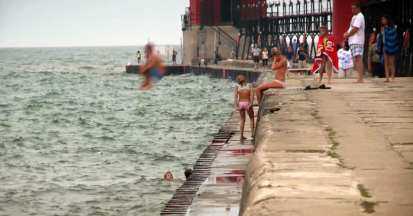 people swimming and jumping off pier into lake michigan