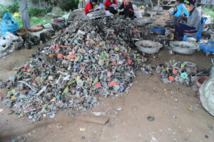 Pile of waste in Thailand with five workers separating metal and plastic components for resale or recycling.