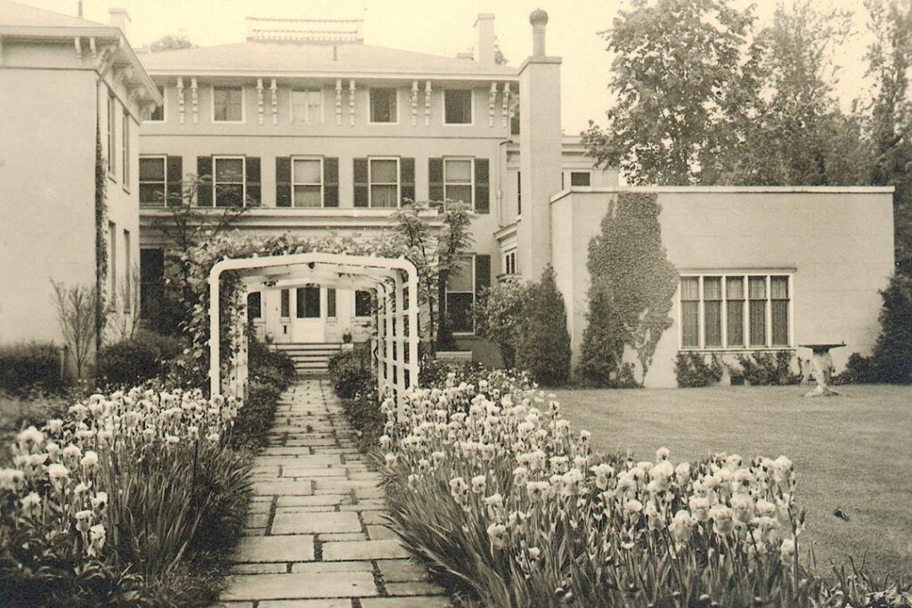 In an undated 20th century photo: A stone walk, flower borders and a tunnel trellis.