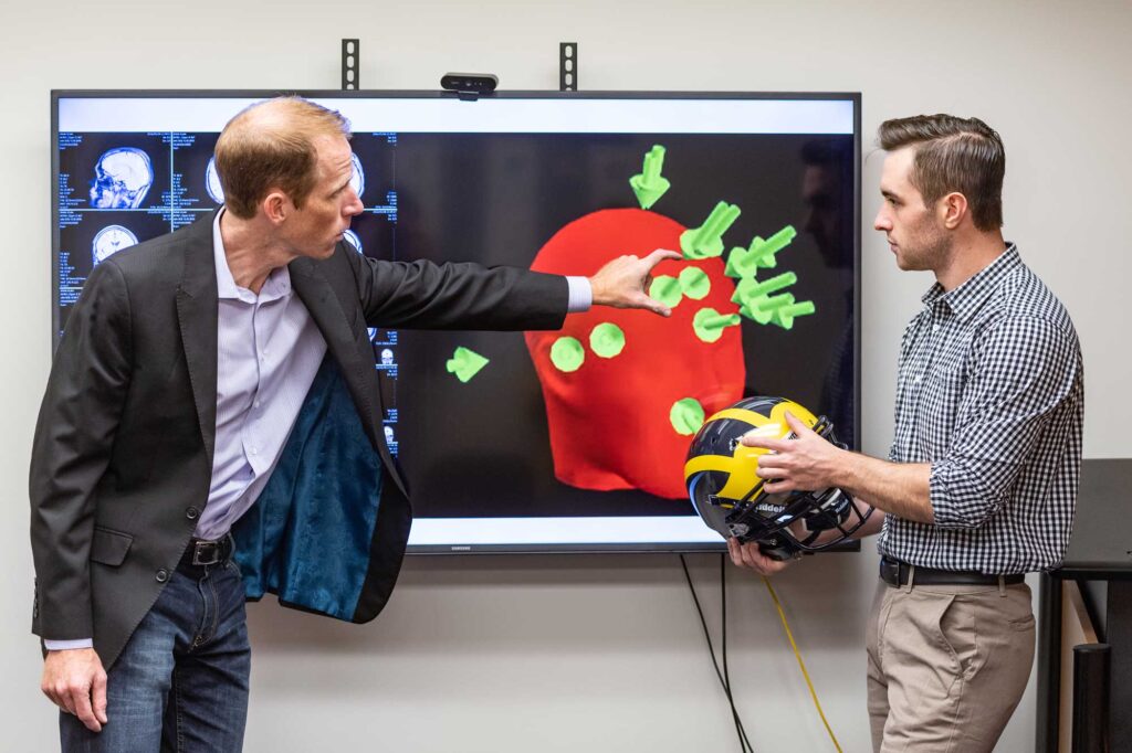 Steven Broglio (left) of the School of Kinesiology and kinesiology student Griffin Feinberg discuss football impact biomechanics and how they relate to brain function. Each arrow indicates a head impact. Image credit: Scott Soderberg, Michigan Photography