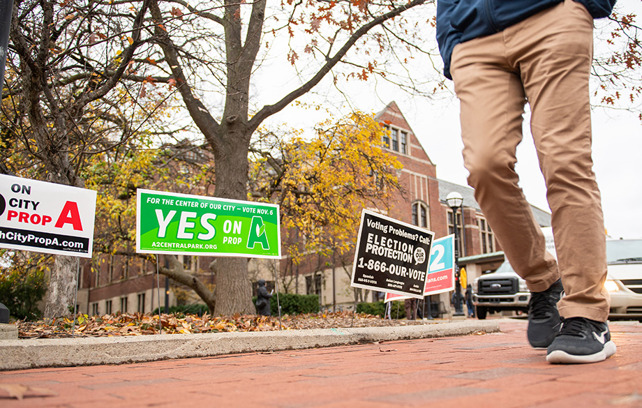 Photo of a person passing campaign signs outside the Michigan Union