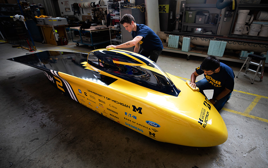 Photo of engineering students Zac Goldsmith, race operations engineer, and Rishabh Goel, race electrical engineer, cleaning the new U-M solar car race vehicle