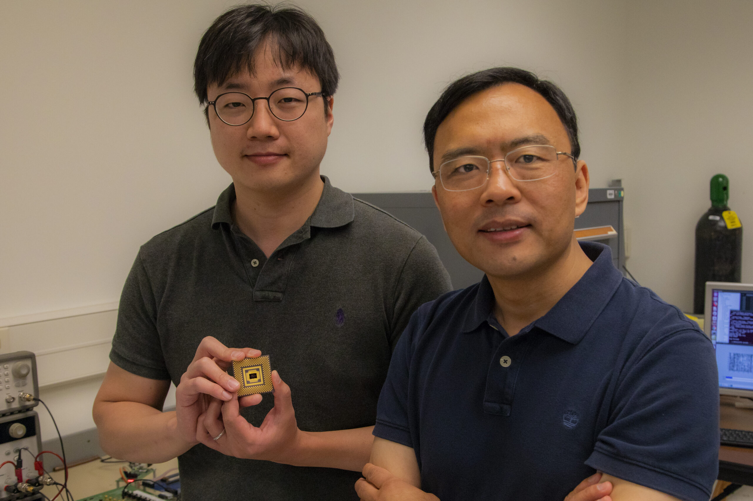 Wei Lu stands with first author Seung Hwan Lee, an electrical engineering PhD student, who holds the memristor array. Image credit: Robert Coelius, Michigan Engineering