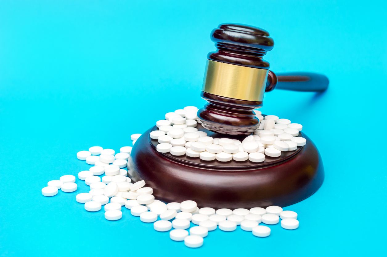 Gavel with white pills on blue. Medical concept. Image credit: iStock