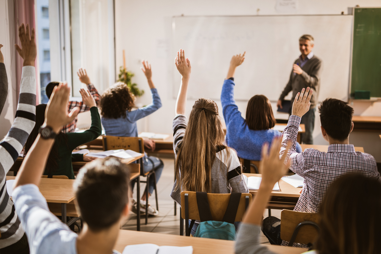 Back view of high school students raising hands on a class. Image credit: iStock