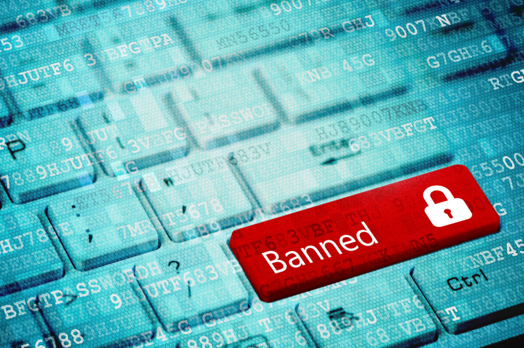 Red key with text Bunned and closed padlock icon on blue digital laptop keyboard. Image credit: iStock Photo