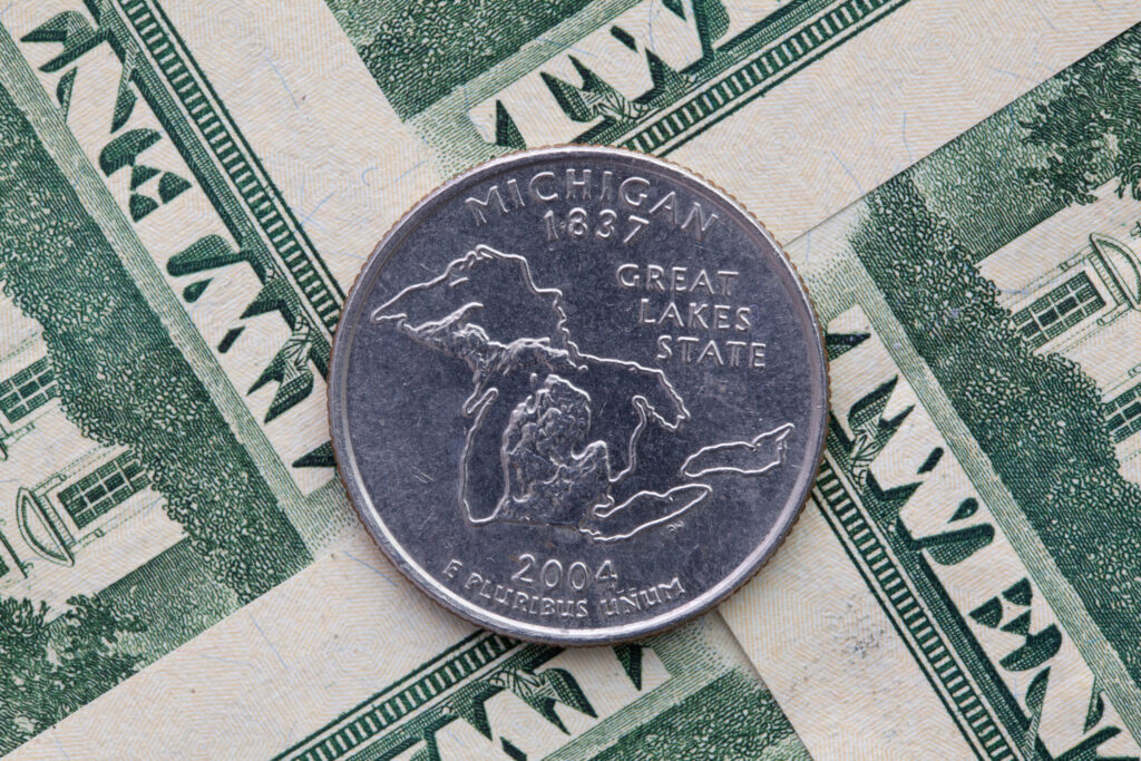 A Michigan quarter sits on several twenty dollar bills. Image credit: iStock