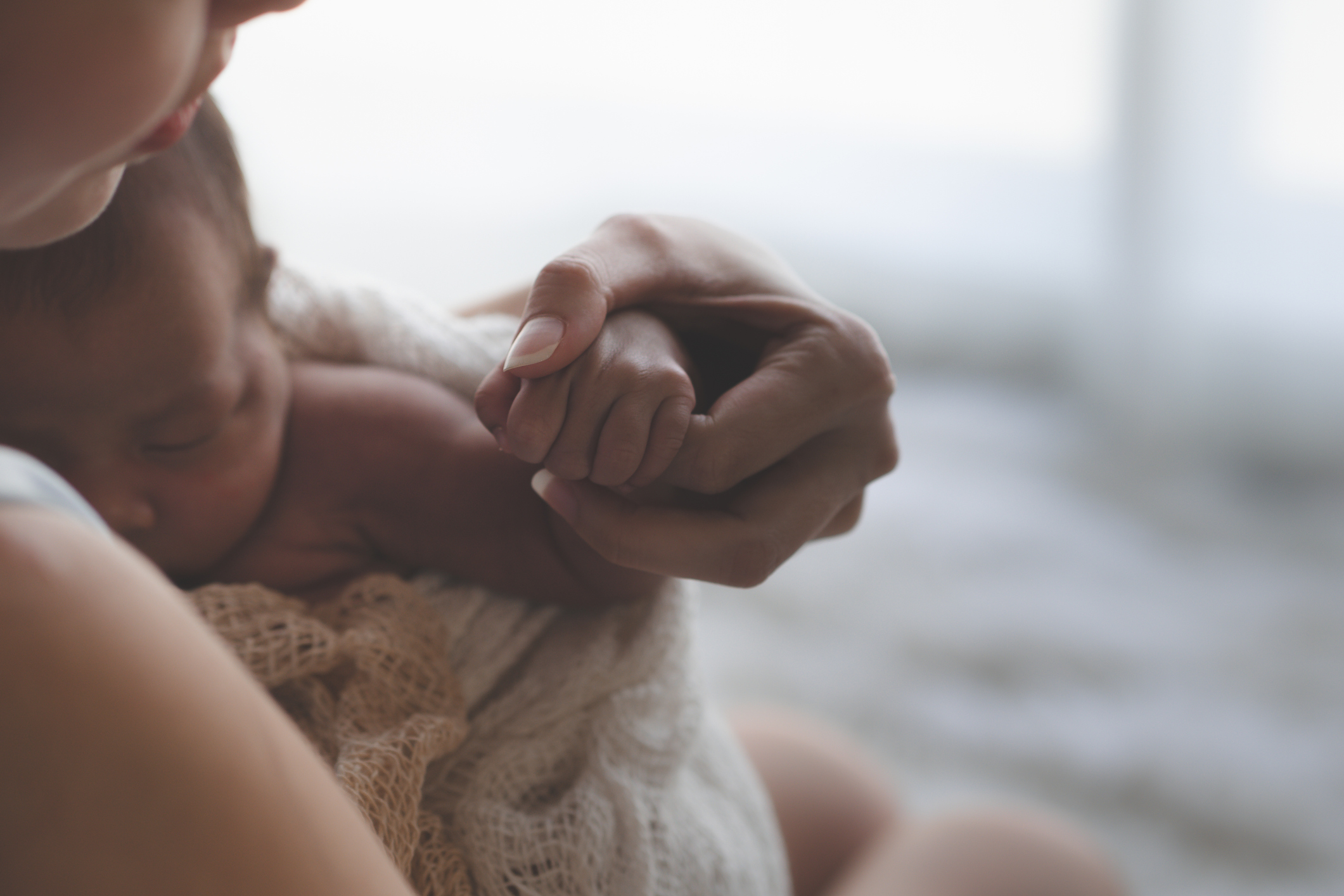 Mother holding newborn baby and holding its hand. Image credit: iStock