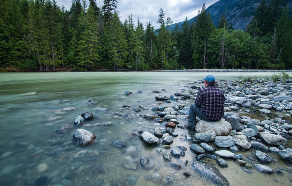 A man sits on a river bank. Image credit: jameswheeler via Pixabay