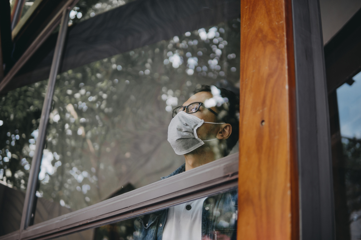 Image of a man in a medical mask behind a window.