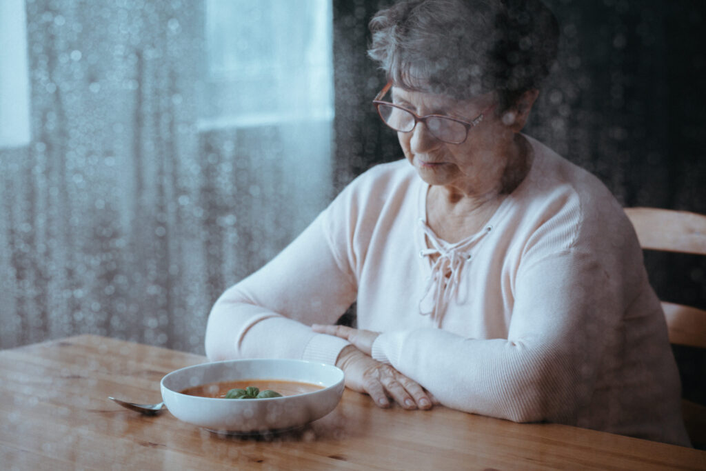 A senior woman gazes at a bowl of food. Image credit: iStock