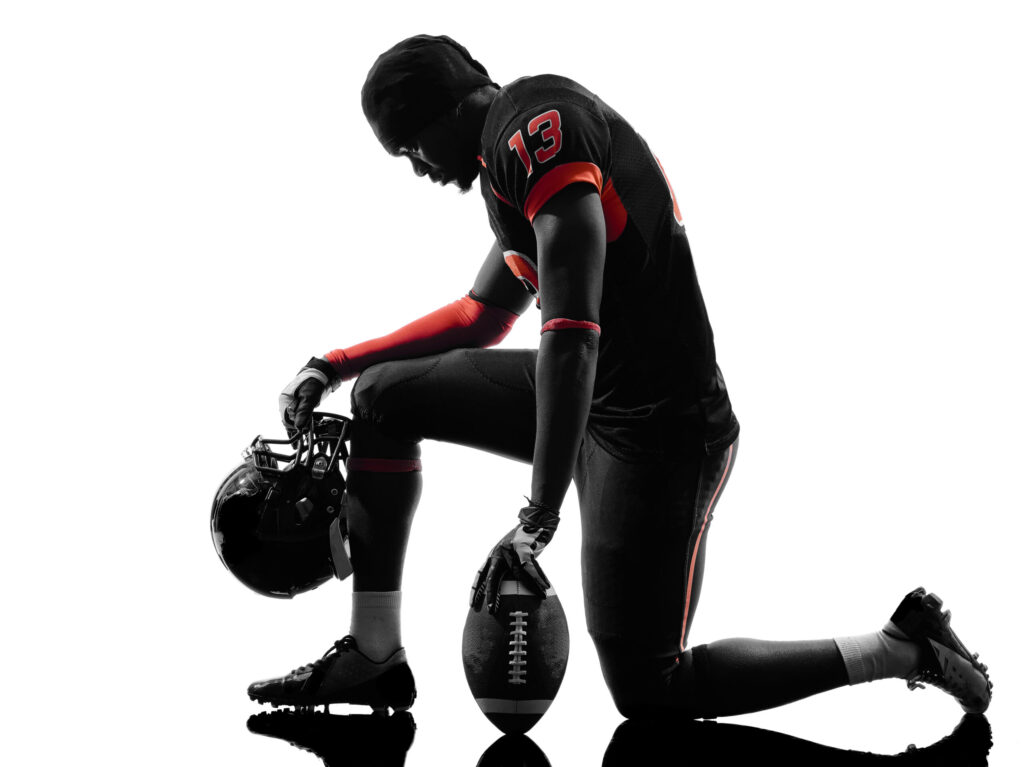American football player kneeling in silhouette shadow on white background. Image credit: iStock