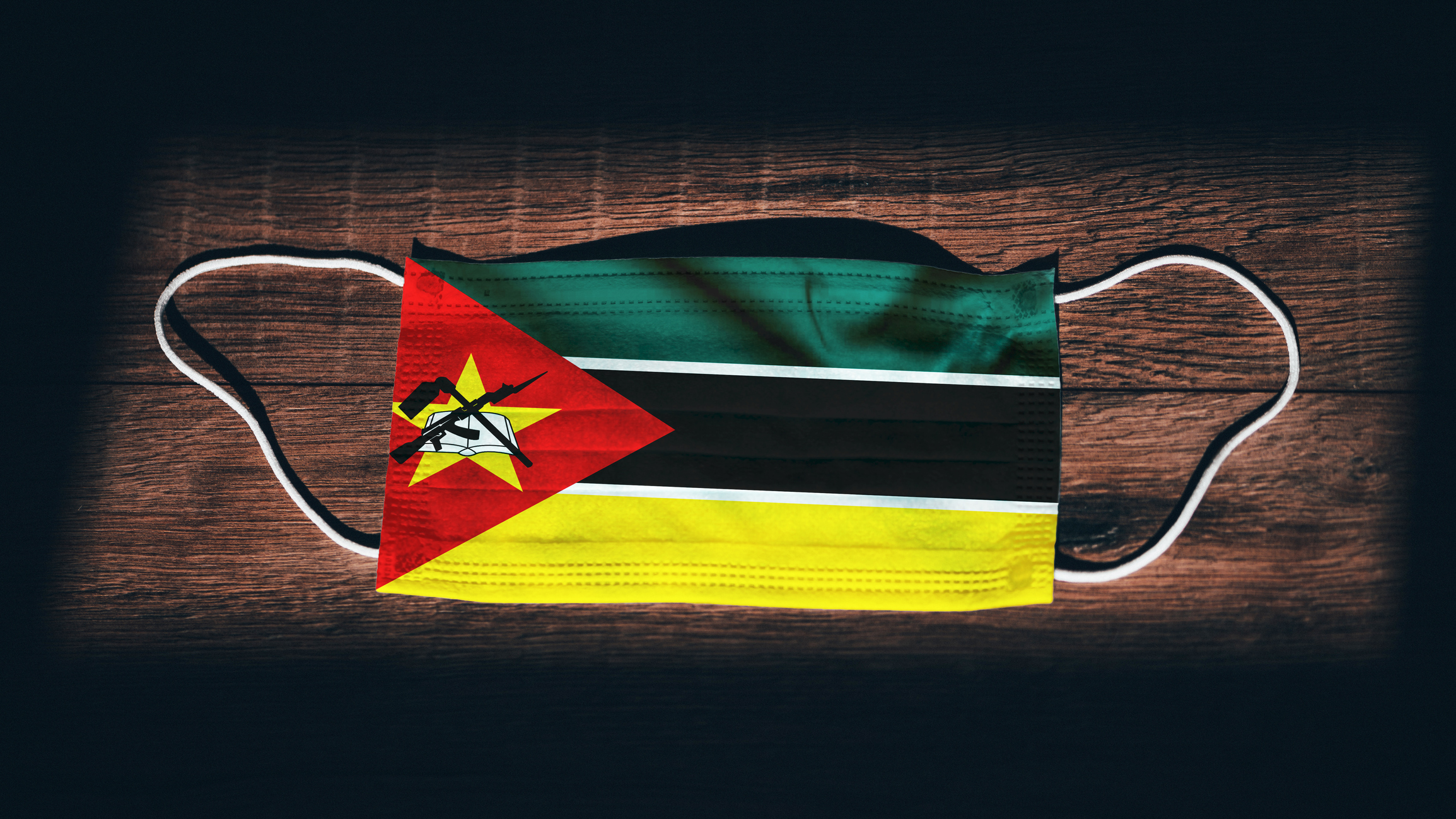 Mozambique National Flag at medical, surgical, protection mask on black wooden background. Coronavirus Covid"u201319, Prevent infection, illness or flu. State of Emergency, Lockdown. Image credit: iStock