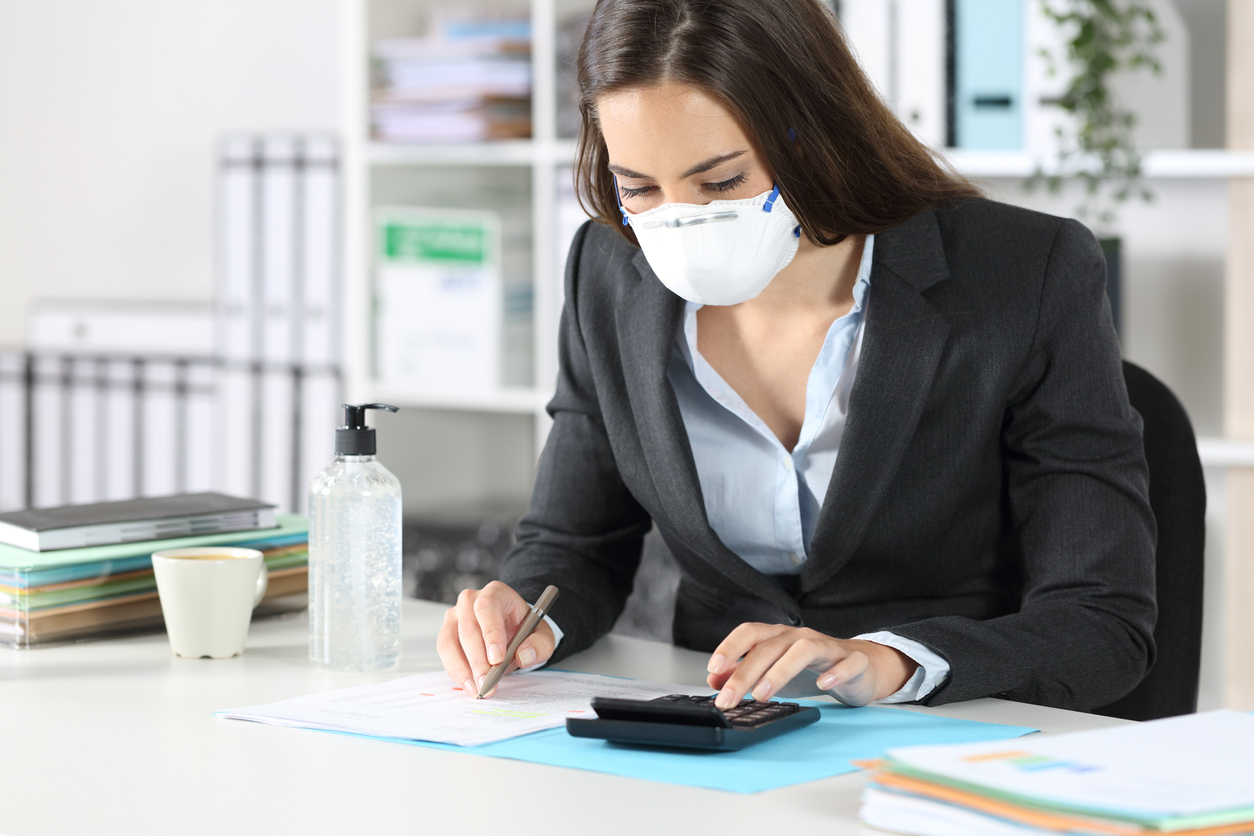 A woman wearing a mask using a calculator. Image credit: iStock