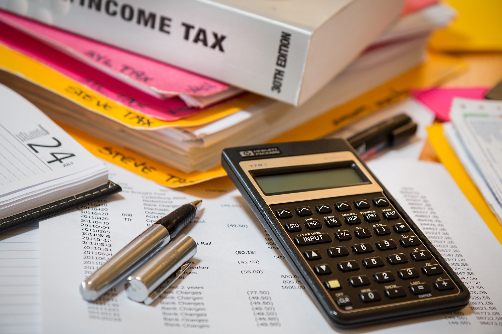 Calculator, papers, binder, and pens on desk. Image credit: pixabay