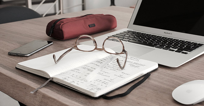 A book, glasses, phone, pencil case, and laptop on a desk. Image courtesy: U-M SPH