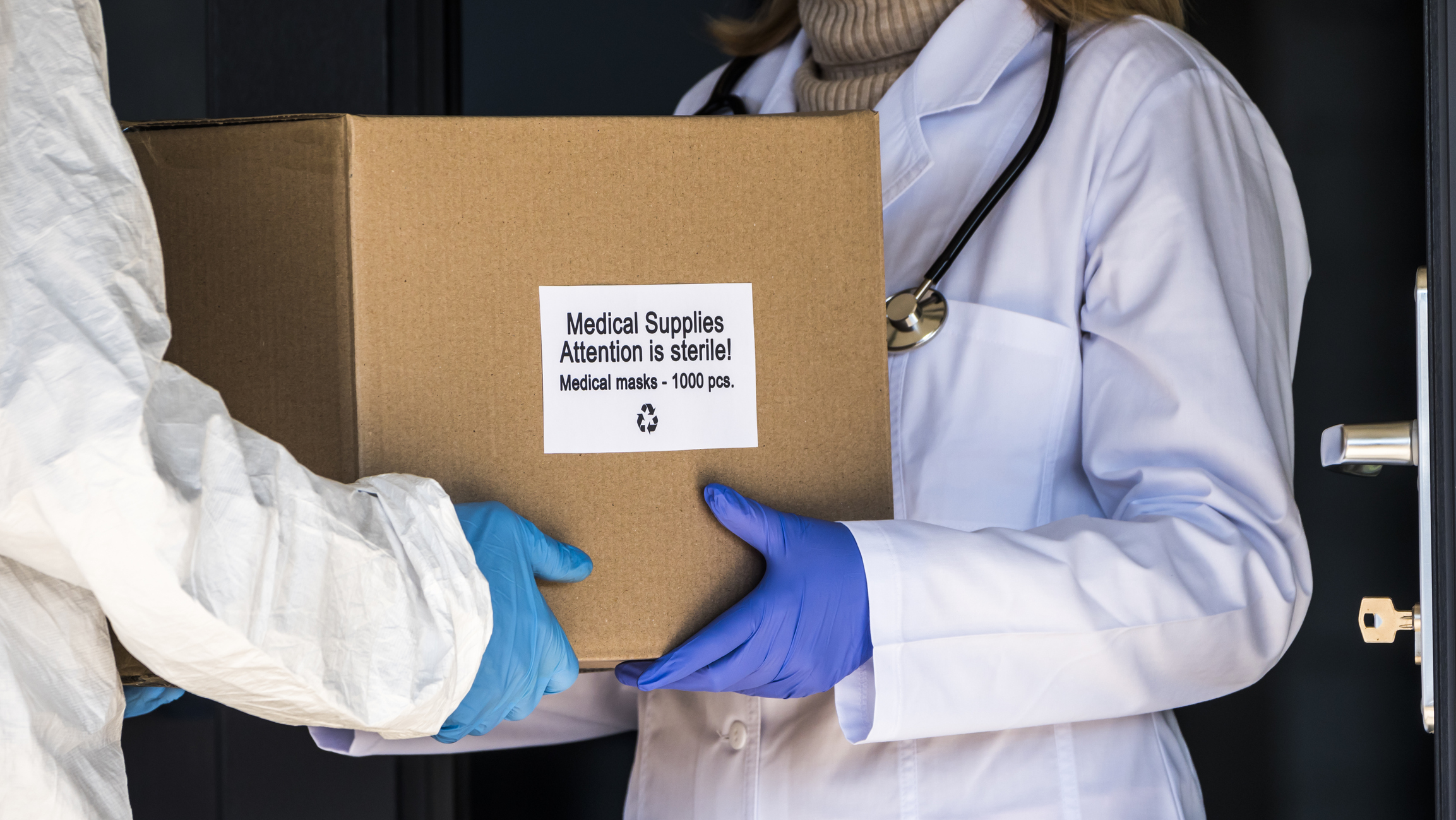 A person in a protective suit is handed a box with protective medical supplies to the doctor. Image credit: iStock