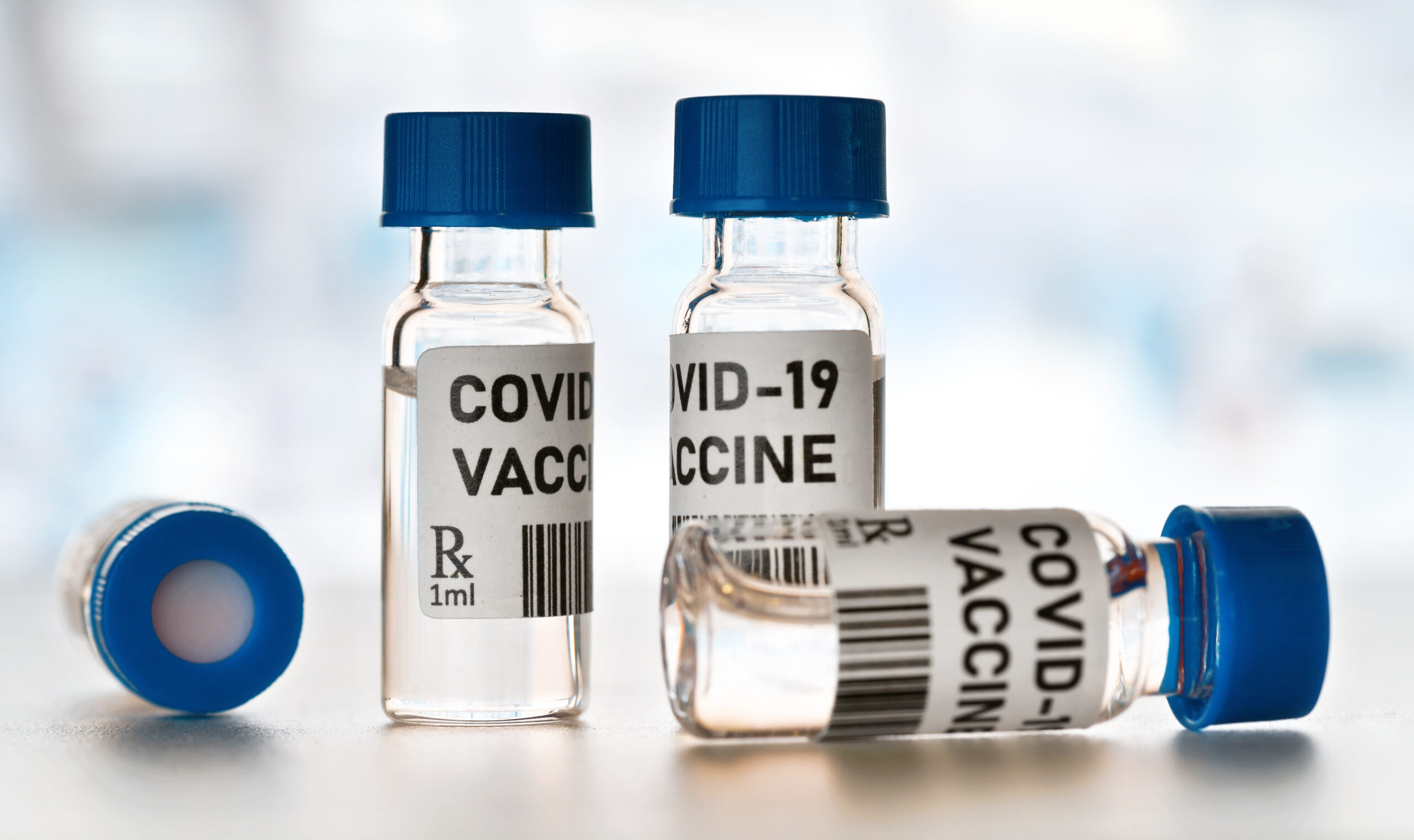 Coronavirus Covid-19 vaccine concept - small glass vials with blue caps on white table, closeup detail (own design - dummy bar code) Image credit: iStock