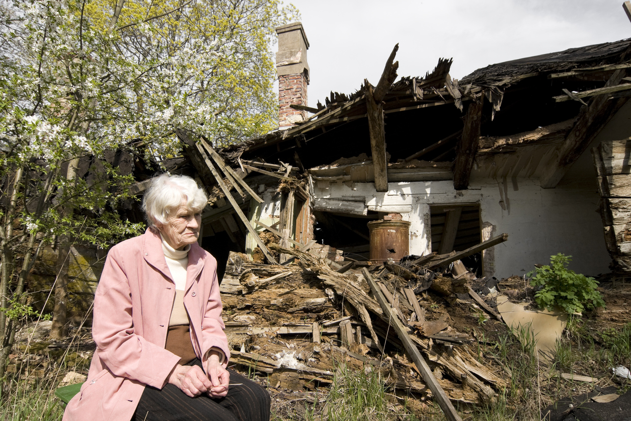 A senior citizen sits outside a destroyed home. Image credit: iStock