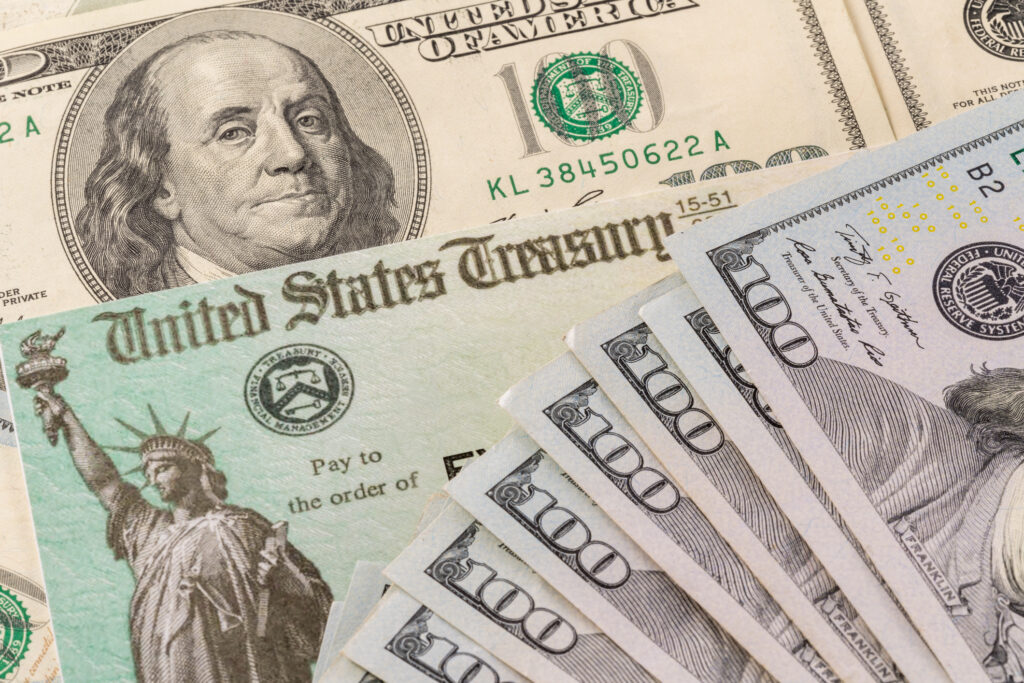 Stack of 100 dollar bills with illustrative coronavirus stimulus payment check to show the virus stimulus payment to Americans. Image credit: iStock
