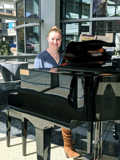 Emily Wheeler, guest services specialist at the Division of Public Safety and Security, sits at the baby grand piano in the lobby of C.S. Mott Children’s Hospital. She has spent many days off from her position to play mostly classical tunes for the visitors, patients and staff at the hospital. (Photo by Jacob Baxter)