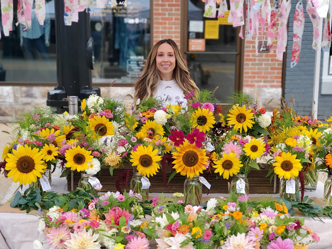 Kasie Meszaros, business administrator for Mcity, poses with her flowers at the Brighton Farmers Market. Meszaros only recently started growing flowers at her Brighton home and sells and gives them away. (Photo courtesy of Kasie Meszaros)