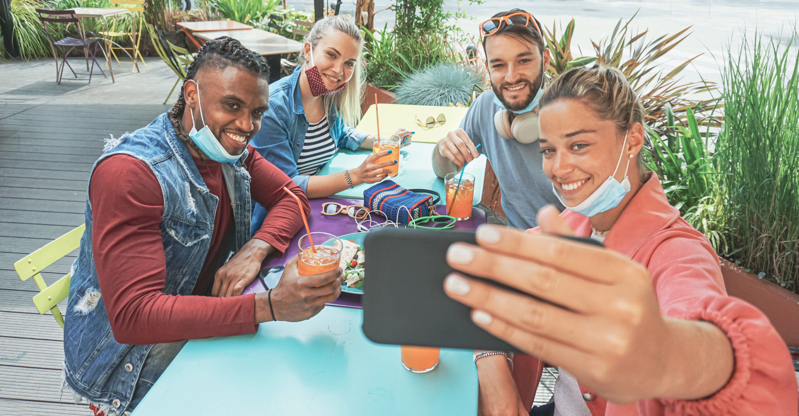 Group of friends at table taking a selfie with masks on their chins.