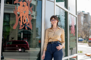 Jenna John, a dual major in art and design and ecology and evolutionary biology at the University of Michigan, poses in front of her installation at Zingerman's Greyline in downtown Ann Arbor. John's work is part of "The art of queer health sciences," an exhibition on view at several downtown Ann Arbor businesses and at queeringart.com. Image credit: Eric Bronson/Michigan Photography.