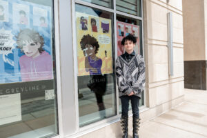 Coyne Gatto, University of Michigan Stamps School of Art & Design student, poses in front of his work at Zingerman's Greyline. Gatto's work is part of "The art of queer health sciences," an exhibition on view at several downtown Ann Arbor businesses and at queeringart.com. Image credit: Eric Bronson/Michigan Photography.
