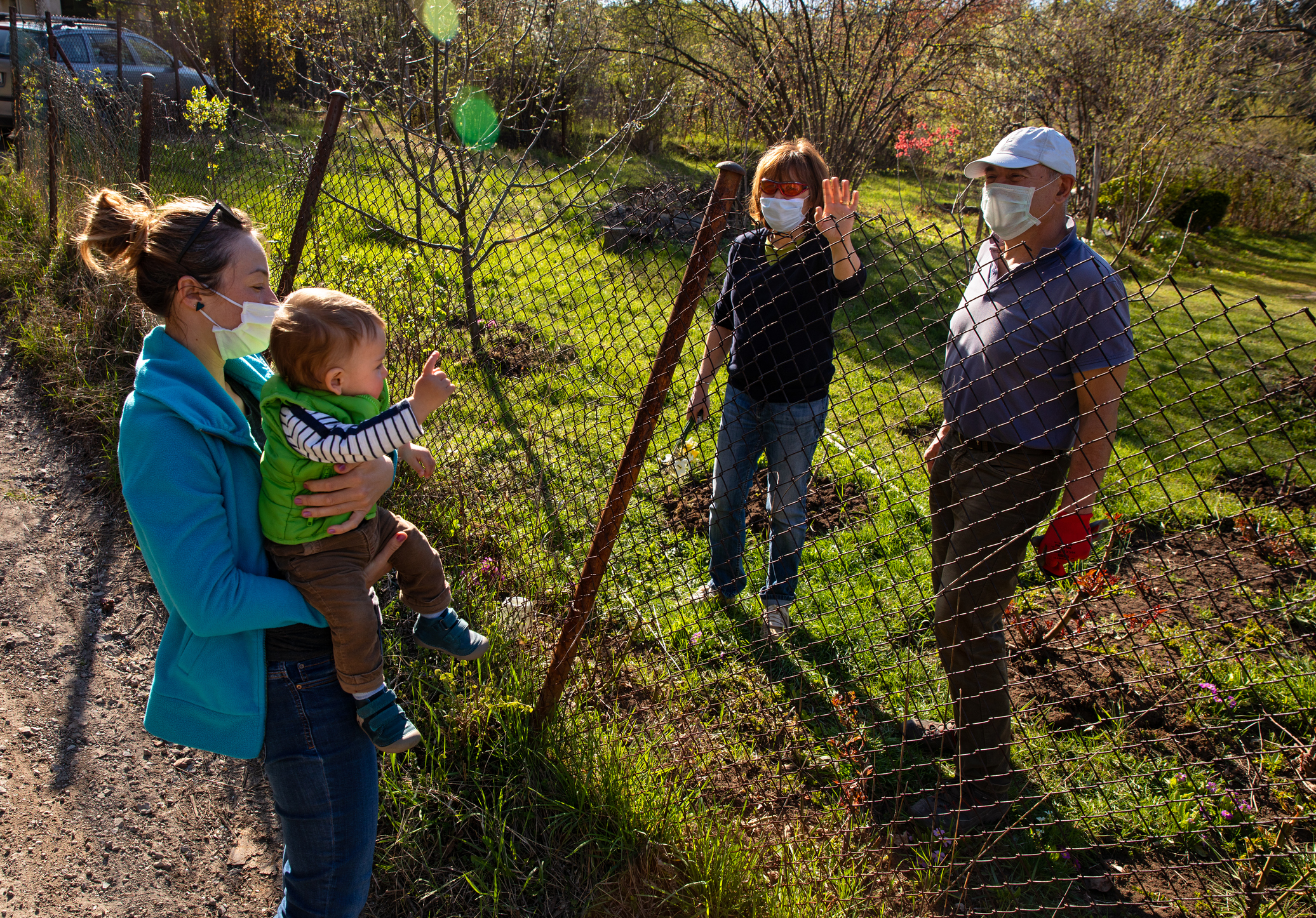 Young mother holding her baby talking with her parents across fence out of the city. Image credit: iStock