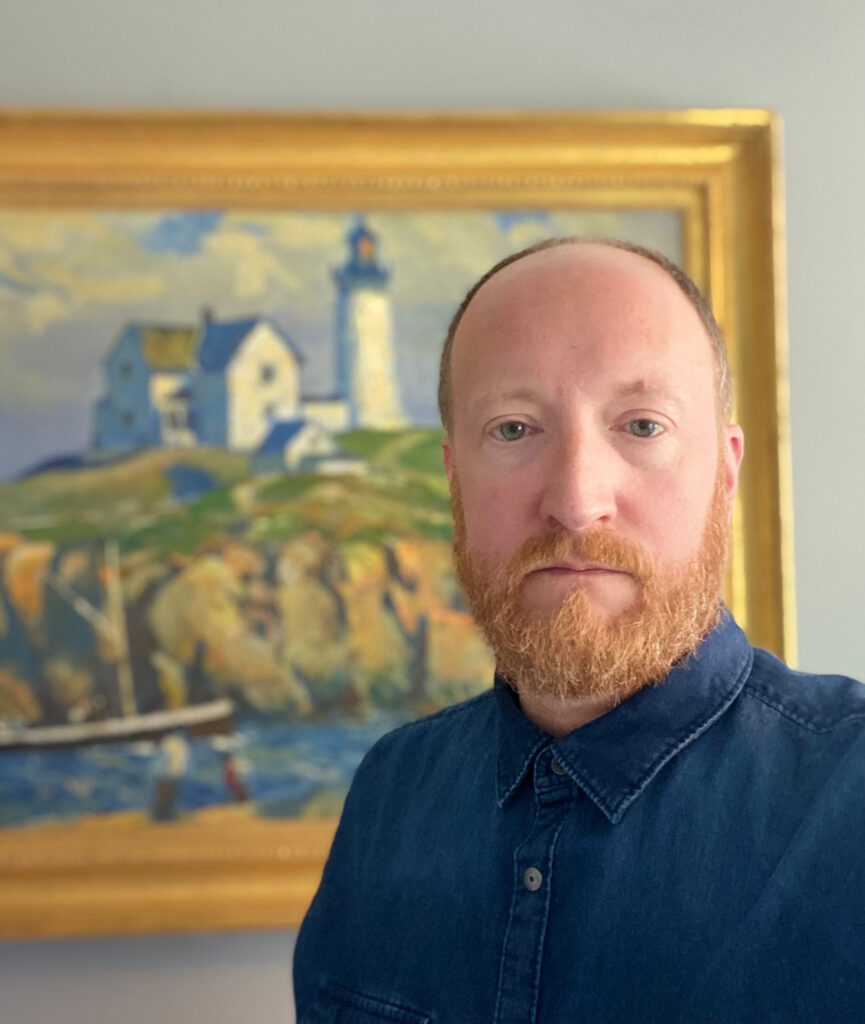 Darin Leese, a business systems analyst for My LINC through Information and Technology Services, poses in front of “Nubble Lighthouse,” a painting by Clarence Chatterton. (Photo by Darin Leese)