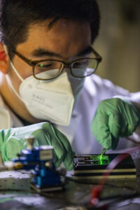 Changyeong Jeong, PhD Candidate in Electrical and Computer Engineering, handles an ultrathin Ag film based OLED inside Professor Jay Guo’s lab at 3537 G.G. Brown on North Campus in Ann Arbor MI on May 5, 2021. Guo’s group is systematically improving the light power distribution in OLEDs by removing the waveguide mode and optimizing the organic stacks and the ultrathin AG anode. This simple yet effective method leads to significantly enhanced performance of the external quantum efficiency of the OLED. Jeong and Guo’s solution is not only simple in process but also can achieve high throughput and low cost with excellent compatibility with the large-scale manufacturing process in the display industry. In principle, the modal elimination approach introduced in this work could be extended to other solid-state light emitting diodes (LEDs) such as perovskites, quantum-dots, or III-V based LEDs since all of which are susceptible to the issue of light trapping as waveguide mode. Image credit: Robert Coelius/University of Michigan Engineering, Communications & Marketing