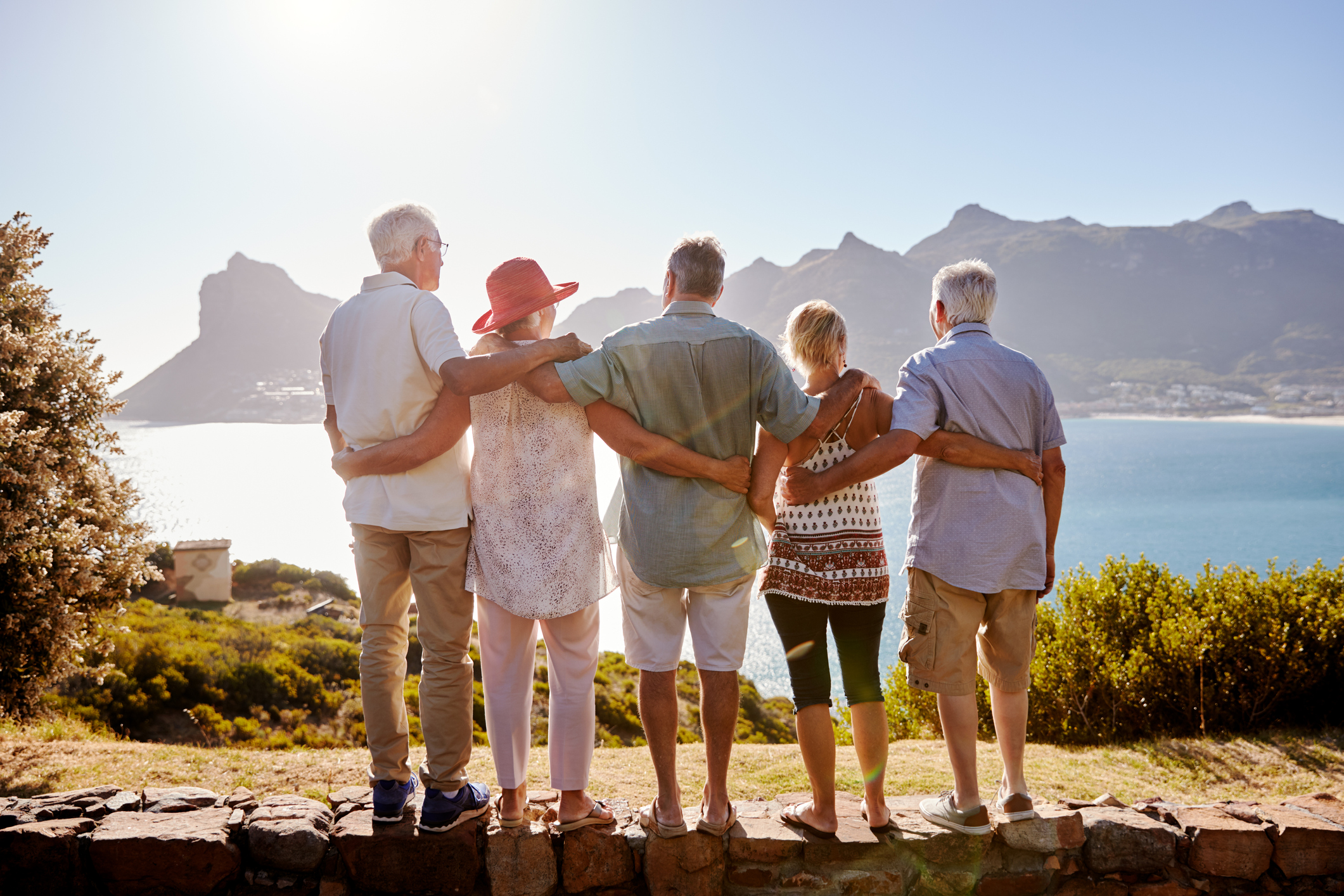 Rear View Of Senior Friends Visiting Tourist Landmark On Group Vacation Standing On Wall. Image credit: iStock