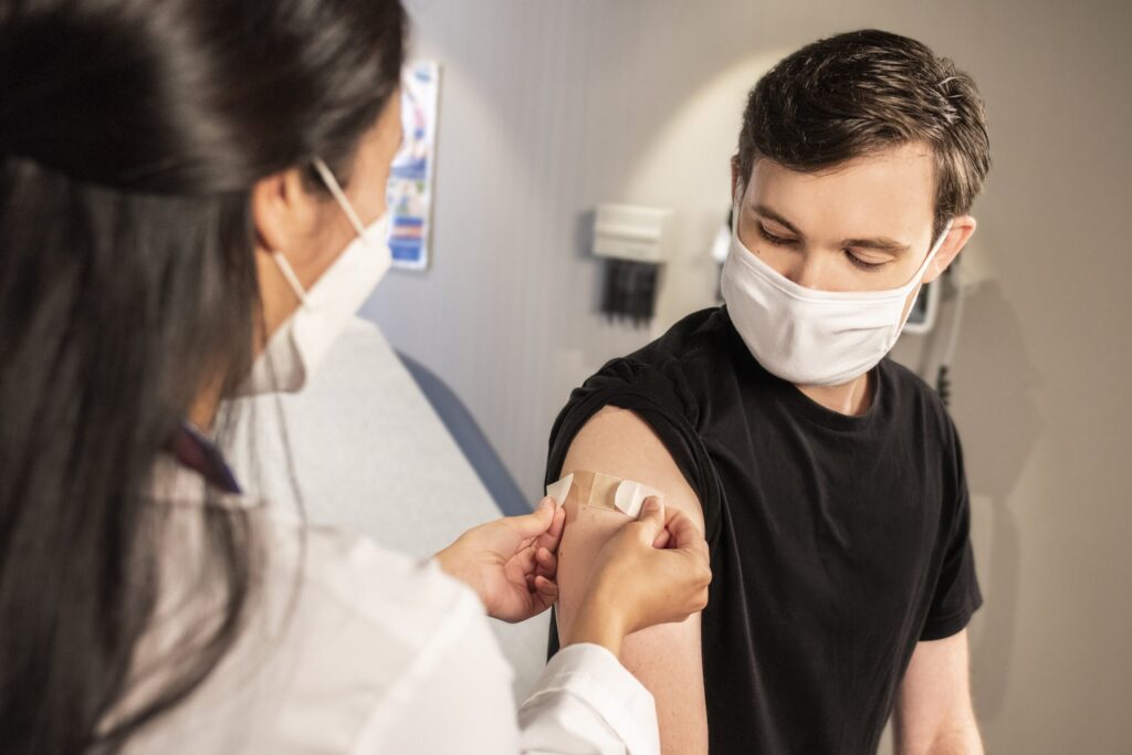 A health care provider placing a bandage on the injection site of a patient after administering the vaccine shot. Image credit: Unsplash.