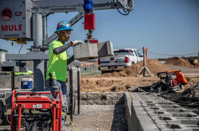 Photo of a construction worker using a robot to place concrete blocks