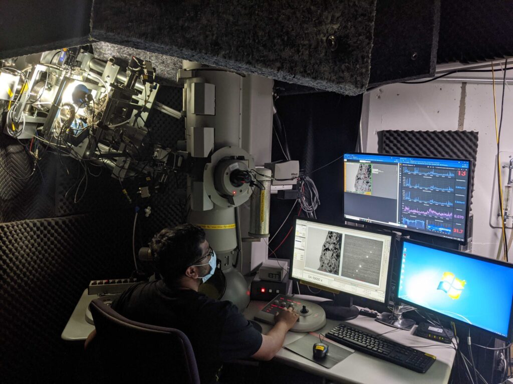 Priyam Patki observes the evolution of the material’s microstructure as irradiation takes place and performs small adjustments to the imaging conditions in the electron microscope. The real-time quantification and visual overlay can be seen in the top monitor where Priyam tries to quantify the number of large “black dot” defects as an evolution of radiation damage. Image credit: Kevin Field, Nuclear Oriented Materials and Examination Group