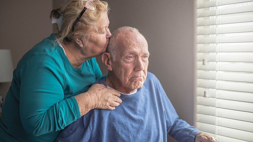 Senior couple kiss forehead window. Image credit: Getty Images