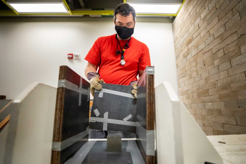 Christopher Meert, a graduate student in nuclear engineering and radiological sciences, arranges the metal shielding that mimics the way weapons-grade uranium and plutonium might be hidden inside shipping containers. During the experiments, he will fire neutrons at material samples inside the box and detect the neutrons and photons when atoms in the sample split, or fission. With a more precise picture of what fissioning uranium and plutonium atoms look like under these conditions, the team will develop algorithms that sift out the noisy data gathered by detectors in the field—to identify the smuggling of materials that could be made into nuclear weapons. Image credit: Robert Coelius, Michigan Engineering