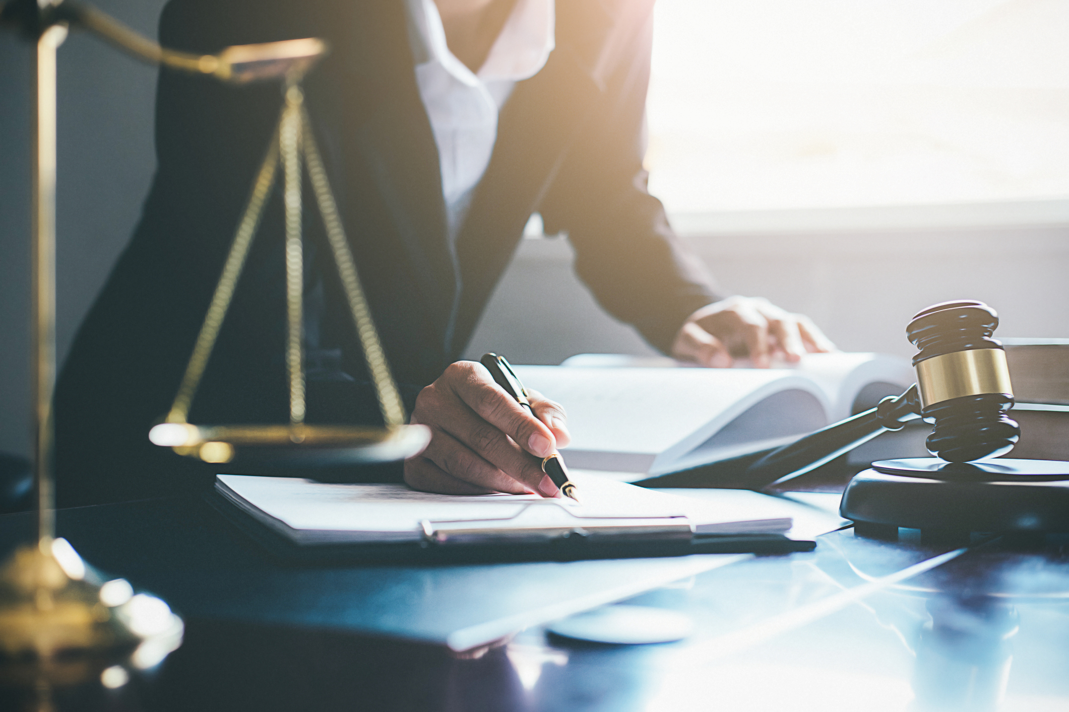 Justice and Law concept. Legal counsel presents to the client a signed contract with gavel and legal law or legal having team meeting at law firm in background. Image credit: MIND_AND_I, iStock