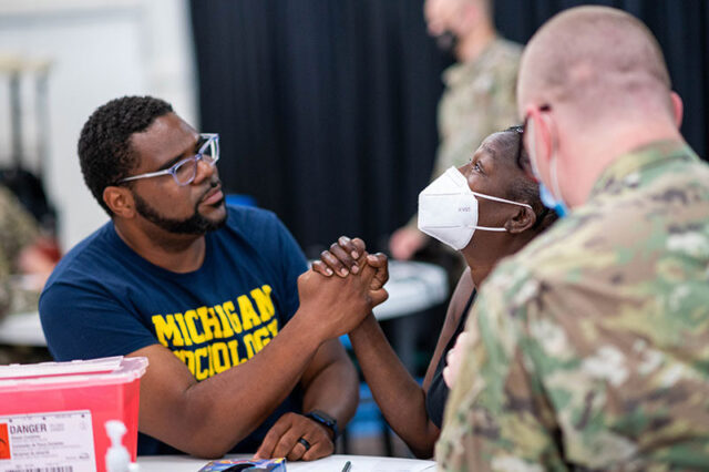 Photo of Charles Williams II holding the hand of a Detroit resident receiving a COVID-19 vaccination at Historic King Solomon Baptist Church.