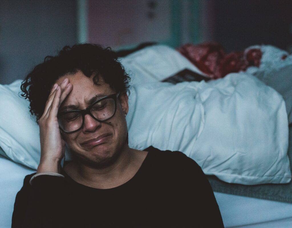 Person crying beside bed. Image credit: Claudia Wolff, Unsplash